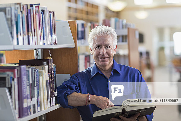 Lächelnder hispanischer Mann mit Buch in der Bibliothek