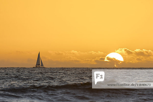 Entferntes Segelboot im Meer bei Sonnenuntergang