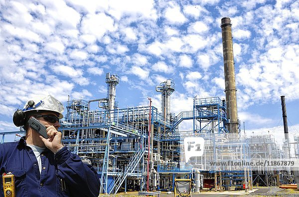 Industriearbeiter in einer Öl- und Gasraffinerie  der ein Mobiltelefon benutzt