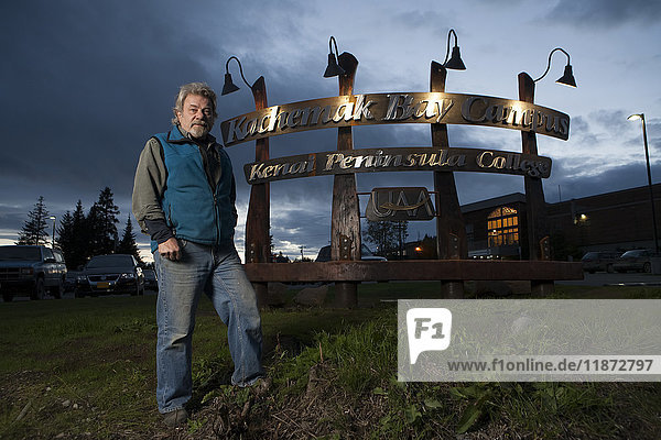 Der Künstler Leo Vait steht mit einem Schild  das er zusammen mit dem Künstler und Schweißer Doug Schweisow für das Kenai Peninsula College Kachemak Bay Campus entworfen und gebaut hat.