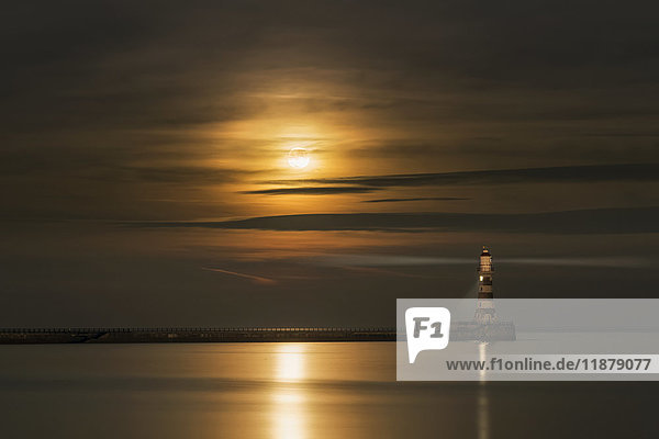 'Roker lighthouse casts a light with the golden sunlight shining through cloud and reflecting on tranquil water; Sunderland  Tyne and Wear  England'
