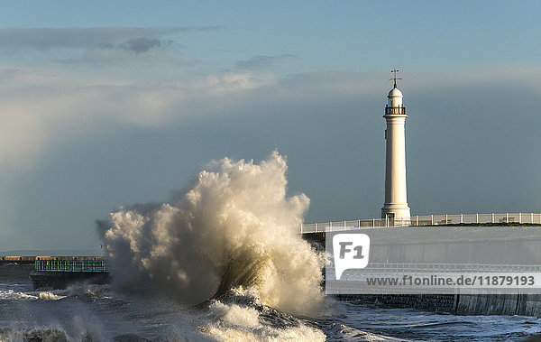 'A large wave crashing against the wall on the shoreline below a lighthouse; Sunderland  Tyne and Wear  England'