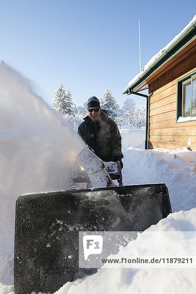 Ein Mann benutzt eine Schneefräse im tiefen Schnee neben seinem Haus; Homer  Alaska  Vereinigte Staaten von Amerika'.