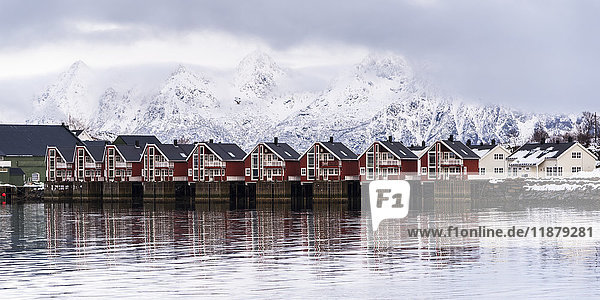 Rote Gebäude am Wasser mit schneebedeckten Bergen im Hintergrund; Svolvar  Lofoten-Inseln  Nordland  Norwegen'.