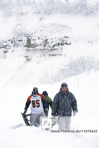 Drei Snowboarder  die mit ihren Snowboards eine Piste im Tiefschnee hinaufgehen; Alaska  Vereinigte Staaten von Amerika'.