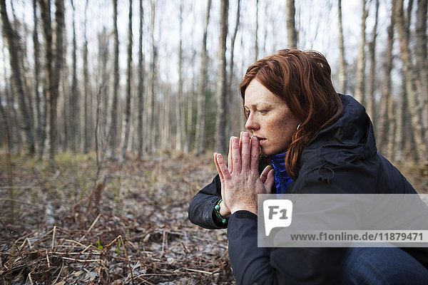 Eine Frau mit roten Haaren hockt auf dem Waldboden und hält die Hände zusammen; Alaska  Vereinigte Staaten von Amerika'.