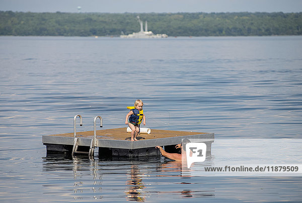 Ein junges kaukasisches Mädchen bereitet sich darauf vor  von einem schwimmenden Steg in die Arme ihres Vaters im Seneca Lake im Bundesstaat New York zu springen; im Hintergrund ist der nicht mehr in Betrieb befindliche Marinekahn zu sehen; Dresden  New York  Vereinigte Staaten von Amerika'.