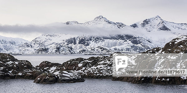 'Snowy landscape of rugged mountains and ocean water; Nordland  Norway'