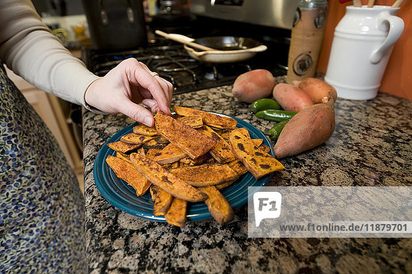 Eine Hand pflückt eine Süßkartoffel von einem Teller in einer Küche; Alaska  Vereinigte Staaten von Amerika'.