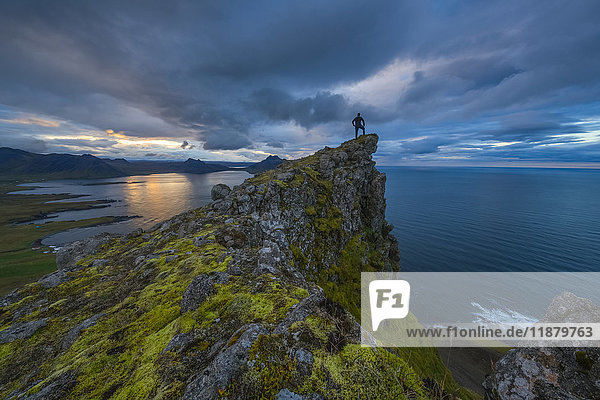 'A person stands and looks at the view from the top of a sea cliff along the Strandir Coast; West Fjords Iceland'