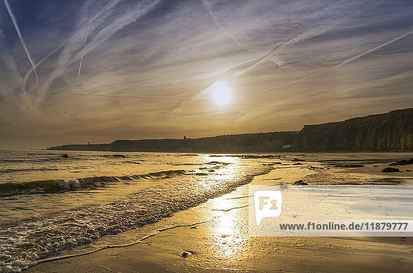 'A sinking sun glows in the sky and reflects off the wet sand along the coast; South Shields  Tyne and Wear  England'