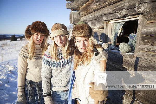 Porträt von drei Mädchen  die an einer Blockhütte stehen und Pelzmützen tragen; Homer  Alaska  Vereinigte Staaten von Amerika'.