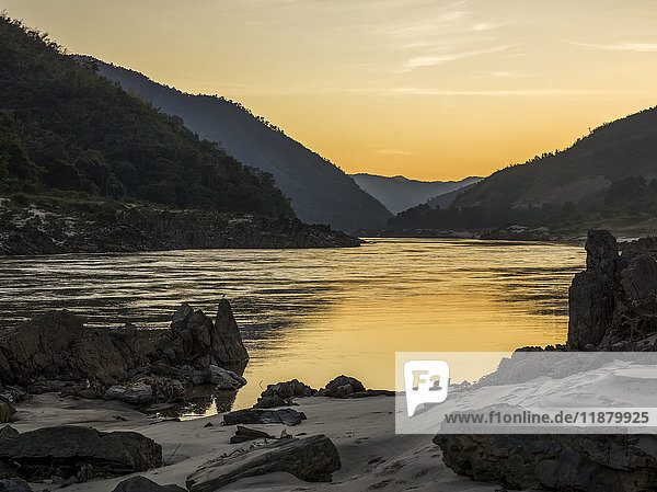 'A golden sunset reflects into the tranquil water with silhouetted mountains; Luang Prabang Province  Laos'