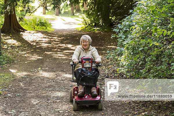 Eine ältere Frau fährt mit einem motorisierten Rollstuhl einen Weg in einem Park hinunter; Yorkshire  England'.