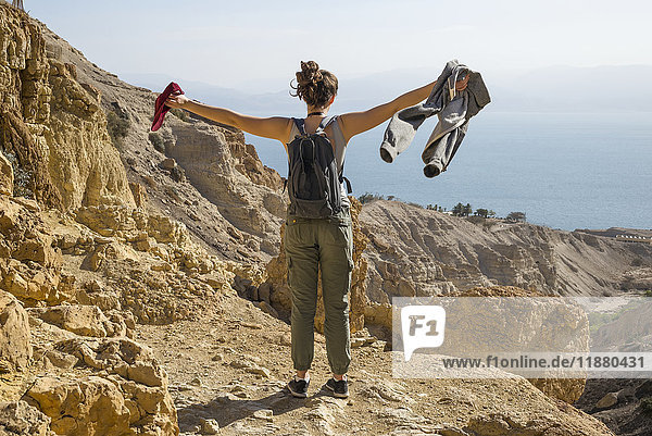 'A young woman stands with arms outstretched at the view of the Dead Sea while hiking in Ein Gedi  Dead Sea District; South District  Israel'