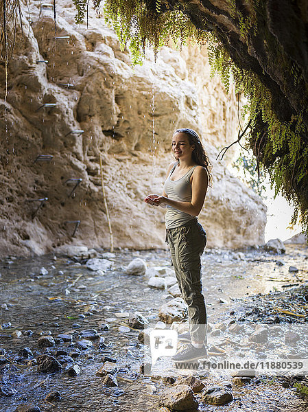'A young woman stands on a rock along a stream at Dodim Cave  Ein Gedi Nature Reserve; South District  Israel'