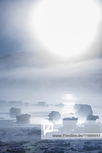 Die Sonne scheint durch den tief liegenden Nebel entlang des Turnagain Arm und des Seward Highway im Winter  das Meereis bedeckt den Ozean im Vordergrund  die Chugach Moutains sind im Hintergrund zu sehen  Süd-Zentral-Alaska; Alaska  Vereinigte Staaten von Amerika'.