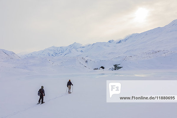 'Two snowshoers approach Canwell Glacier in the Alaska Range on a winter day; Alaska  United States of America'