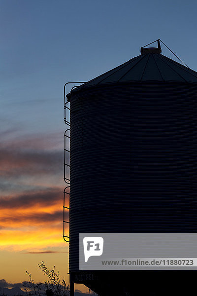 Silhouette eines großen Getreidesilos aus Metall mit bunten Wolken bei Sonnenuntergang und blauem Himmel; Alberta  Kanada'.