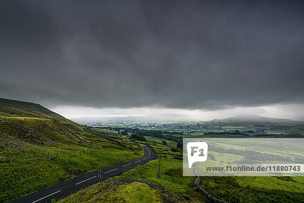 Dark storm clouds over a lush  green landscape and road; North Yorkshire  England