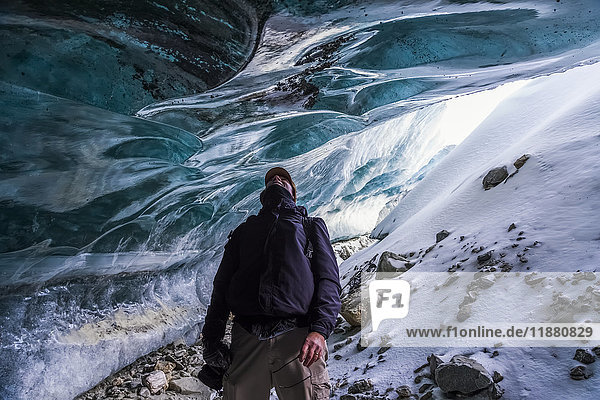'A man looks up at the ice of Canwell Glacier while standing in the entrance to an ice cave; Alaska  United States of America'