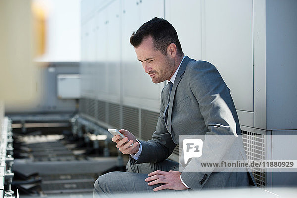 Geschäftsmann sitzt im Freien und schaut auf sein Smartphone