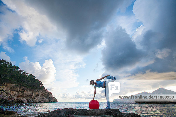 Frau mit Medizinball auf Felsen stehend  Palma de Mallorca  Islas Baleares  Spanien  Europa