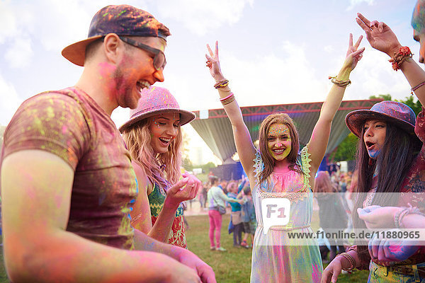 Young adult friends dancing covered in coloured chalk powder at festival
