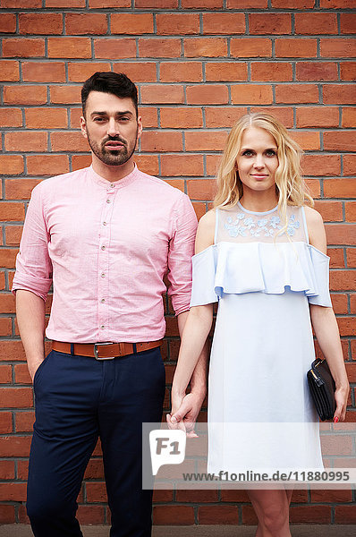 Portrait of couple holding hands in front of brick wall
