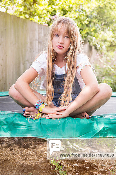 Porträt eines Mädchens  das auf einem Trampolin sitzt und in die Kamera schaut