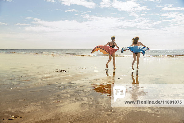 Mutter und Tochter laufen am Strand mit Schals in der Luft  Folkestone  UK