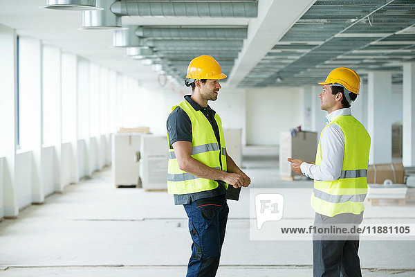 Zwei Männer in Hi-Vis-Weste bei einer Diskussion in neu errichteten Büroräumen