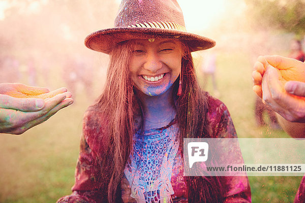 Hände bedecken junge Boho-Frau mit farbigem Kreidepulver beim Festival