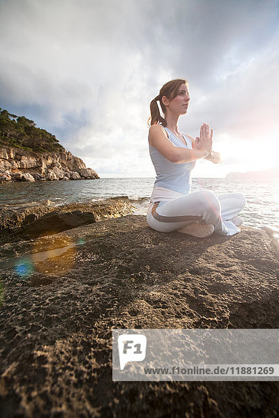 Woman sitting on rocks by sea hands together meditating  Palma de Mallorca  Islas Baleares  Spain  Europe