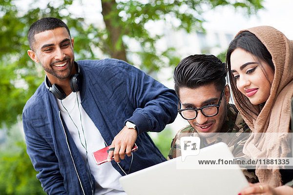 Three friends outdoors  looking at laptop