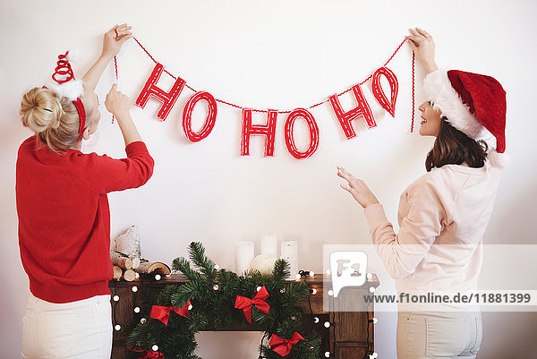 Rear view of two young women putting up christmas decorations on wall