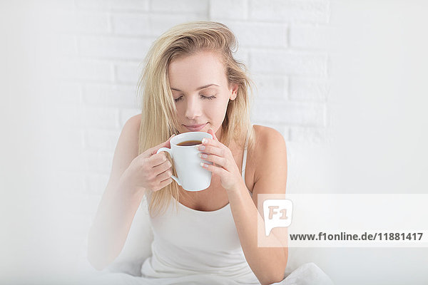 Young woman holding coffee cup  eyes closed  slowly waking up