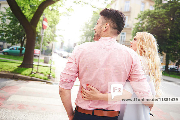 Rear view of couple walking in street arms around each other