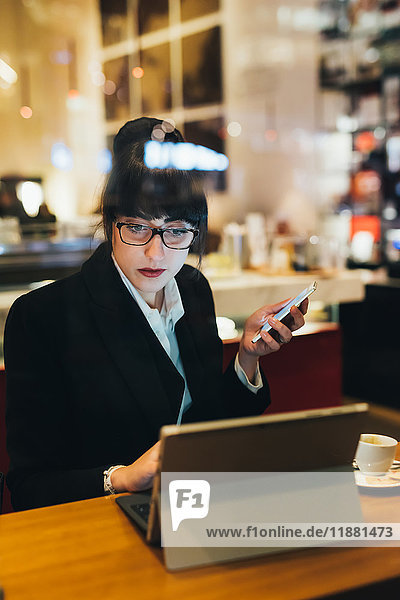 Businesswoman using mobile phone and digital tablet in cafe