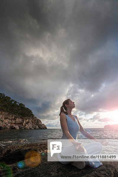 Frau sitzt auf Felsen am Meer und meditiert  Palma de Mallorca  Islas Baleares  Spanien  Europa