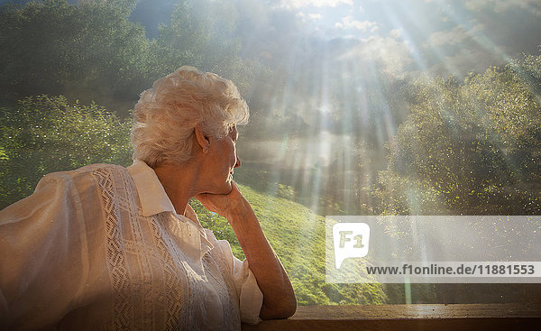 Ältere Frau betrachtet entspannte ländliche Szene vom Fenster einer Eigentumswohnung aus