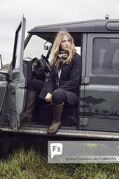 Young woman looking out from off road vehicle door in field