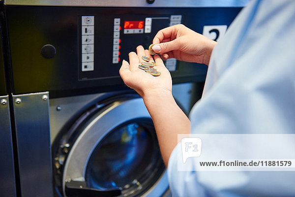 Hände einer Frau  die im Waschsalon Münzen für die Waschmaschine auswählt