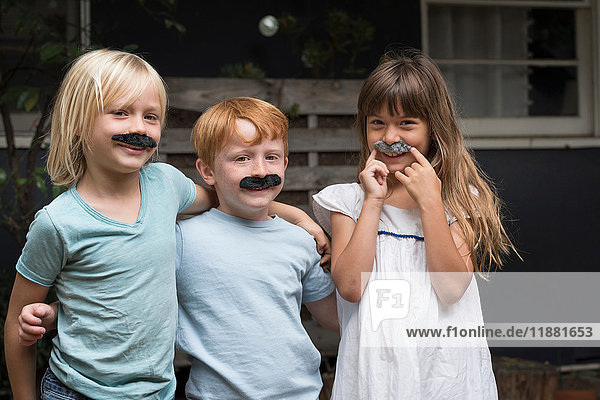 Children wearing fake mustaches looking at camera smiling