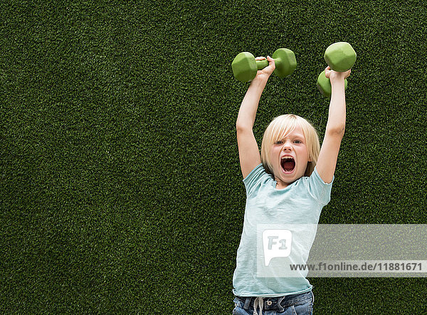 Boy in front of artificial grass lifting dumbbells