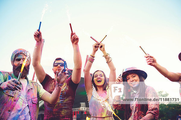Junge Erwachsene mit farbigem Kreidepulver bedeckt  die beim Festival mit Wunderkerzen tanzen
