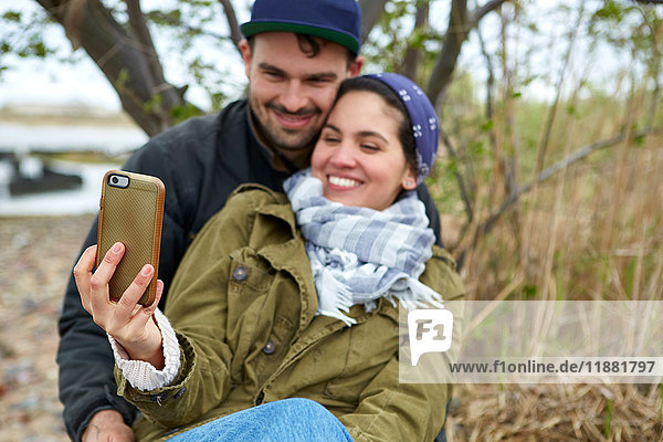 Glückliches junges Paar mit Smartphone-Selfie am Strand