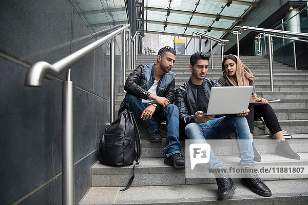 Drei Freunde  die auf Stufen sitzen und auf den Laptop schauen