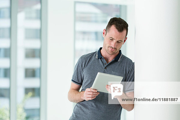Man leaning against wall  looking at digital tablet