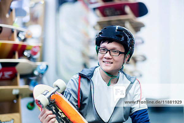 Junger männlicher Skateboarder hält Skateboard in Skateboardladen